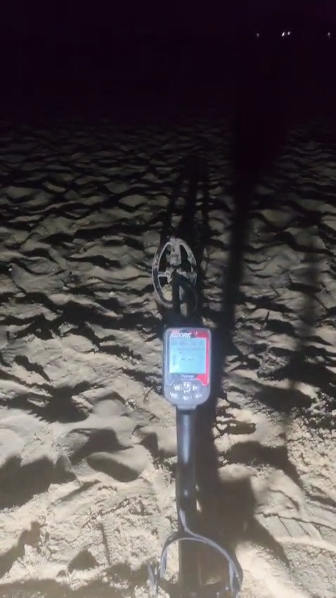 A metal detector resting on the dry sand of Praia da Falésia at night during the search