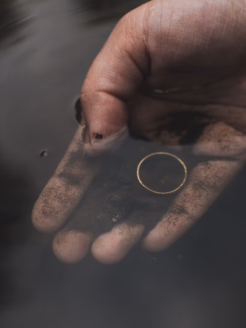 Ein schlichter Goldring auf einer sandigen Hand, knapp unter der Wasseroberfläche