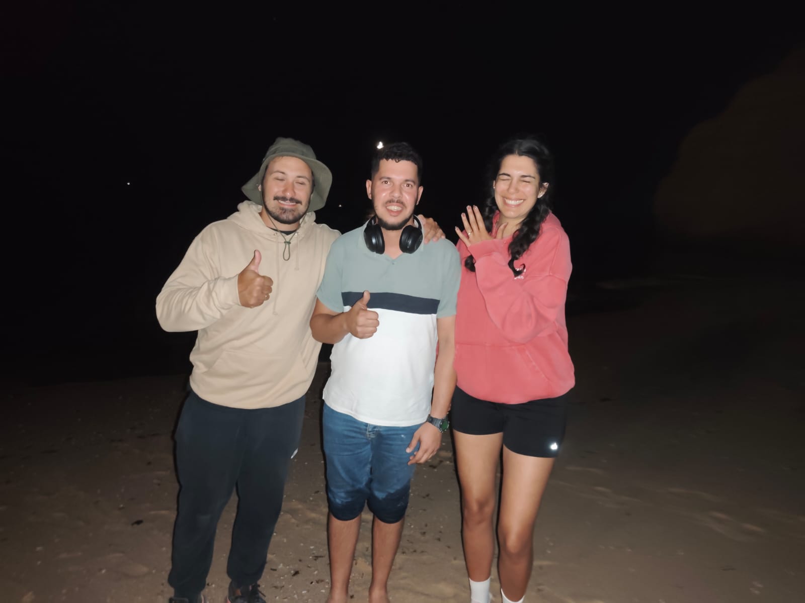 Öznur, her husband and our detectorist on the sand at Vale Centeanes at night, Öznur holding up her hand with the engagement ring back on her finger