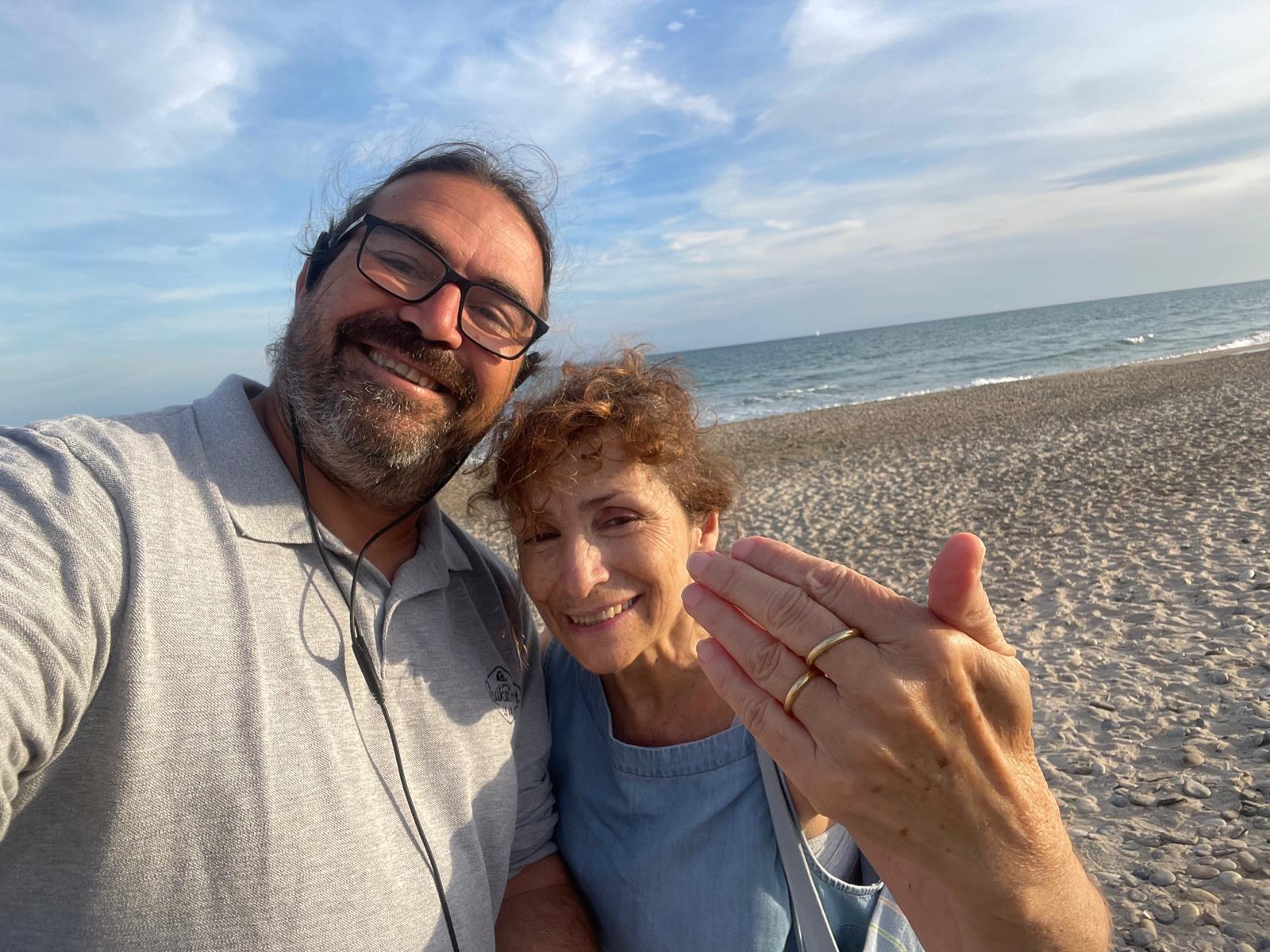 A smiling man and woman on Plage du Pilou near Palavas-les-Flots, the woman holding up her hand to show the recovered gold wedding ring, with the sea behind them