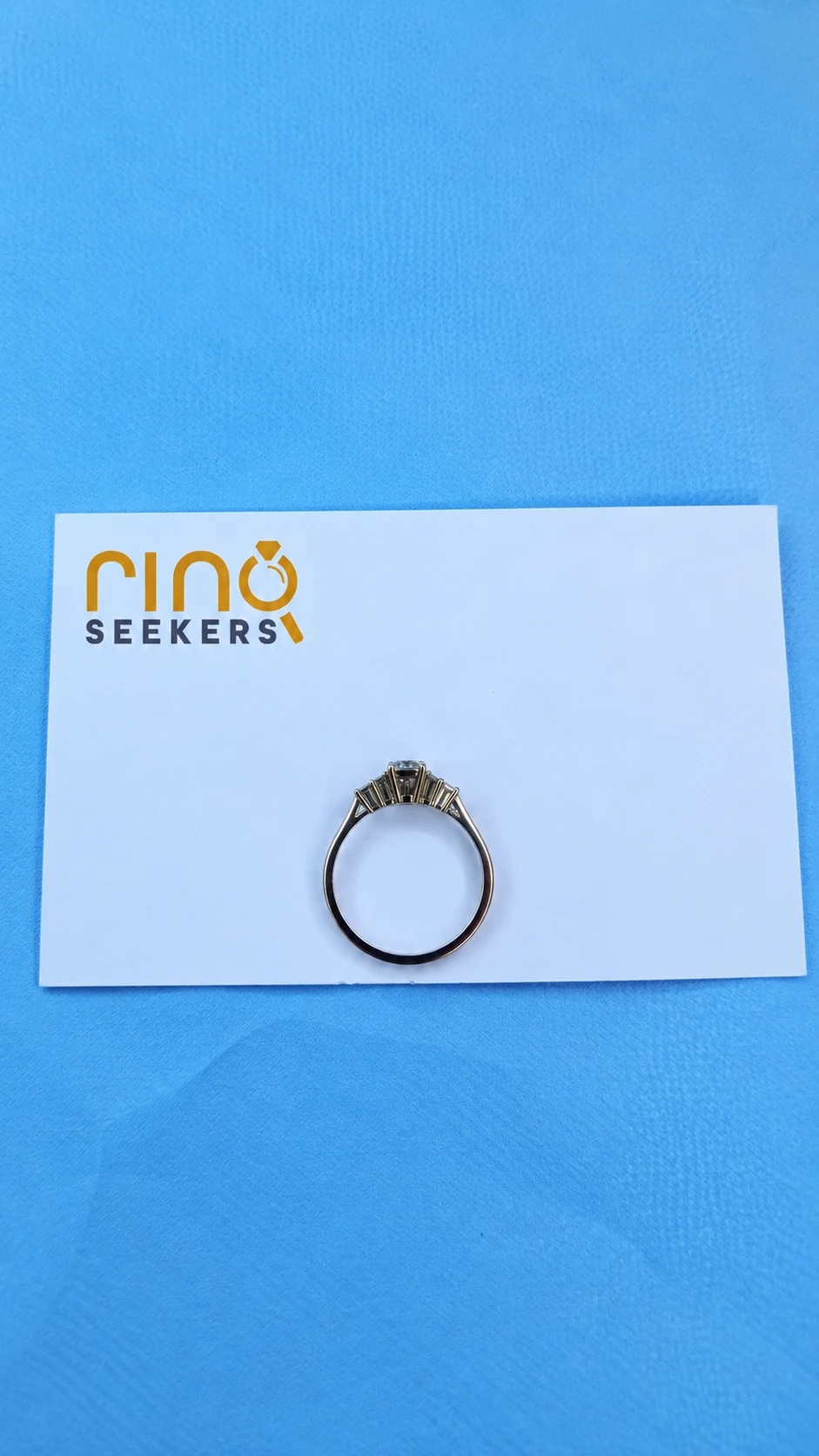 The recovered gold ring with a row of small diamonds, standing on a Ring Seekers card on a blue cloth