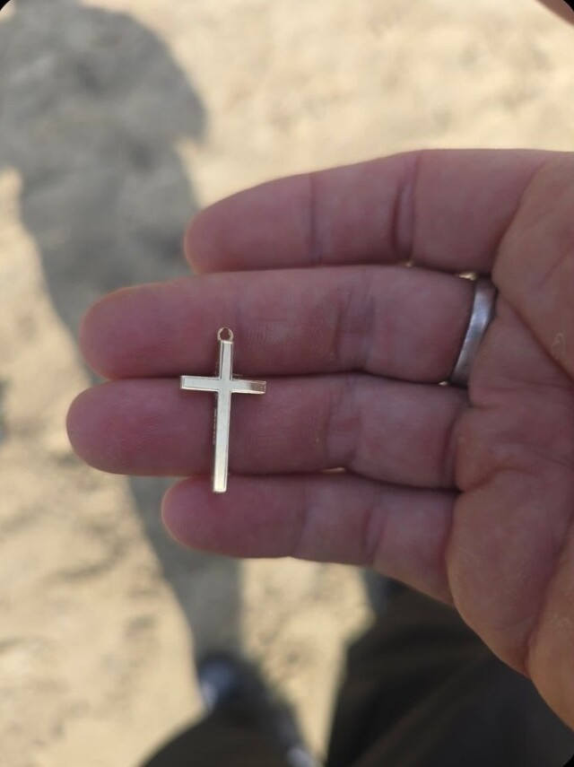 The small gold cross pendant resting on the detectorist's open hand above the sand at Sandsfoot Beach in Weymouth, just after it was found with a metal detector
