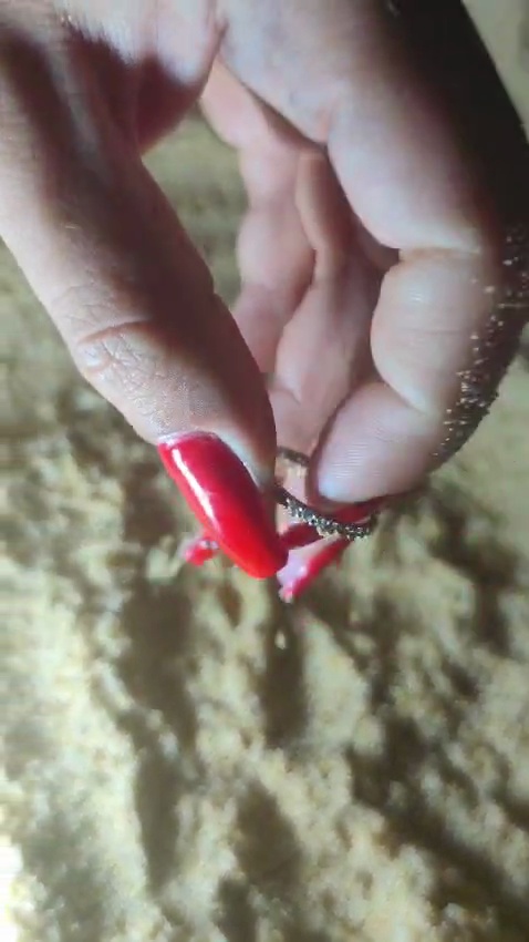 Fingers lifting the diamond wedding ring out of the dry sand at Praia da Falésia at night, lit by a torch