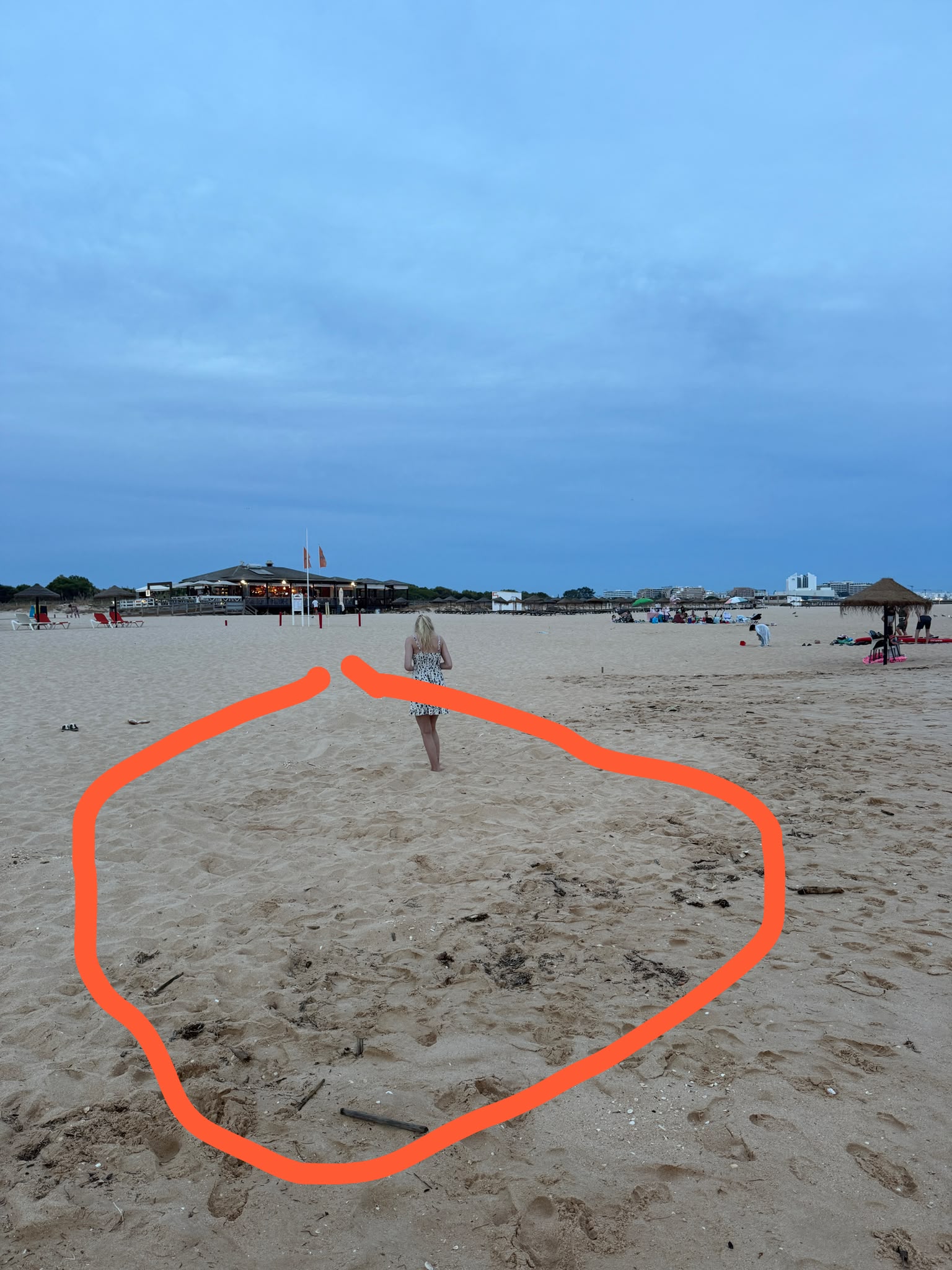 Praia da Falésia at dusk with the beach restaurant behind and an orange circle drawn on the sand where the ring was lost