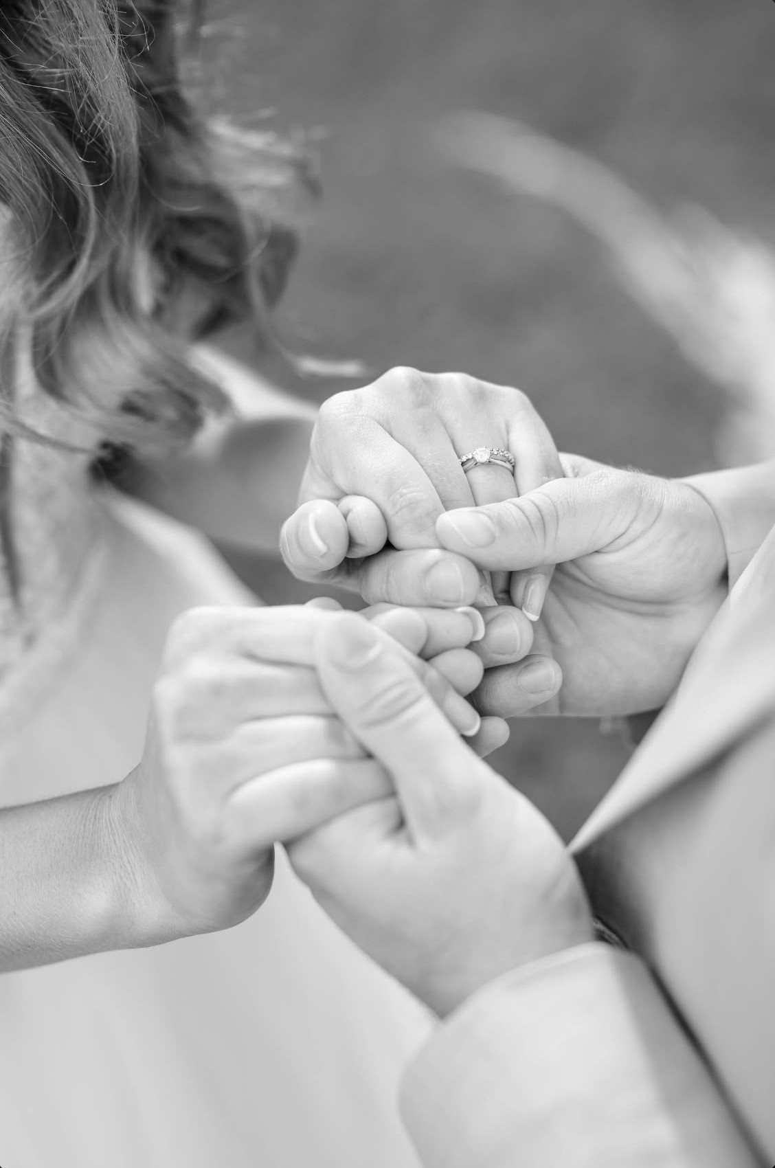 Black and white wedding photo of a bride and groom holding hands, her wedding ring and engagement ring on her finger