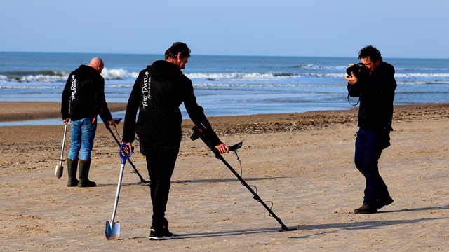 A metal detector coil held low and level, just above the surface of the sand