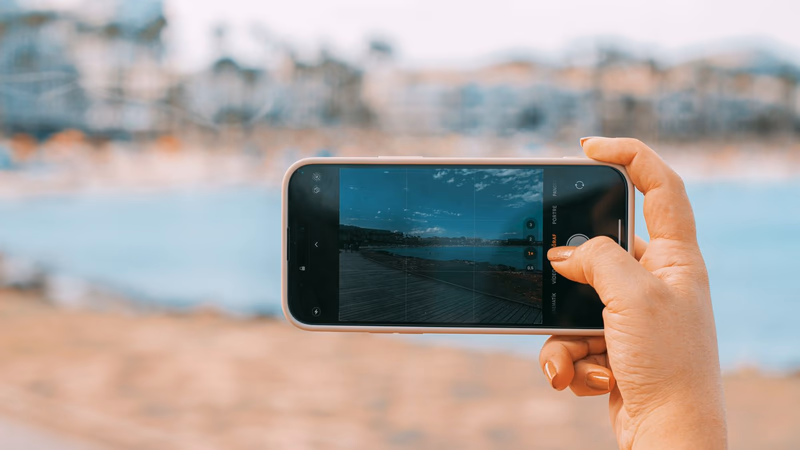 A hand holding up a phone in front of a beach, ready to message a ring finder after losing a ring