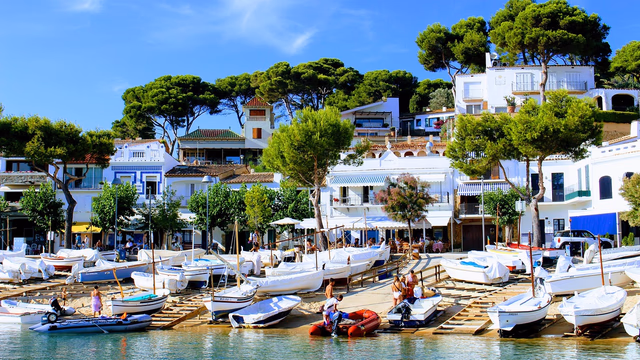 A small Costa Brava cove with pine trees above the rocks and clear turquoise water over sand and pebbles, the kind of beach where a lost ring settles among stones