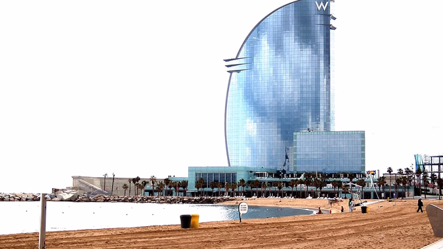 Early morning light on the wide sand of Barceloneta beach in Barcelona with the sea beyond, the kind of busy city beach where a lost ring is raked over every night