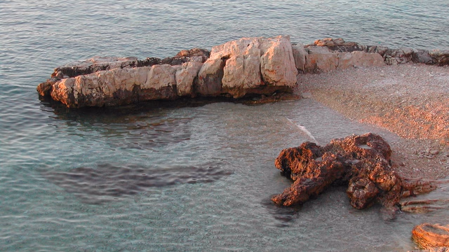 A pebble beach beside clear turquoise sea on a rocky summer coastline, the kind of beach where a lost Pandora bracelet or silver charm is searched for with a metal detector